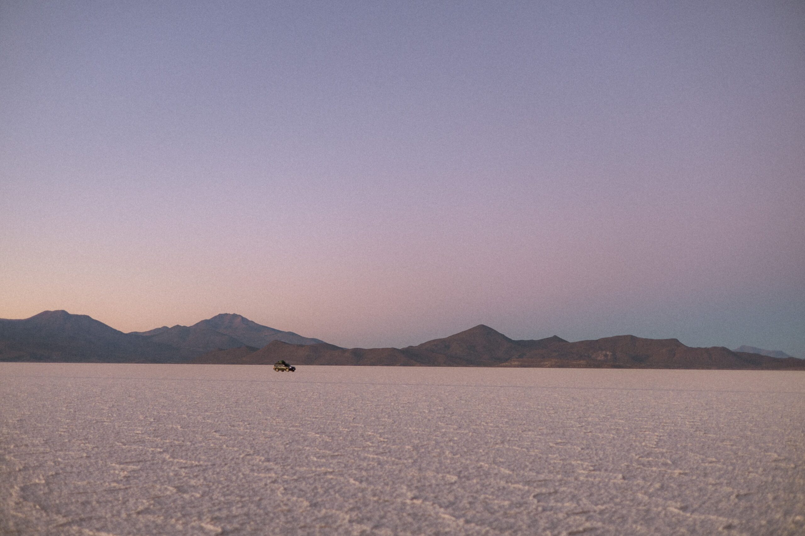Breathtaking sunrise over Bolivia's Salar de Uyuni with a distant vehicle and mountain backdrop.