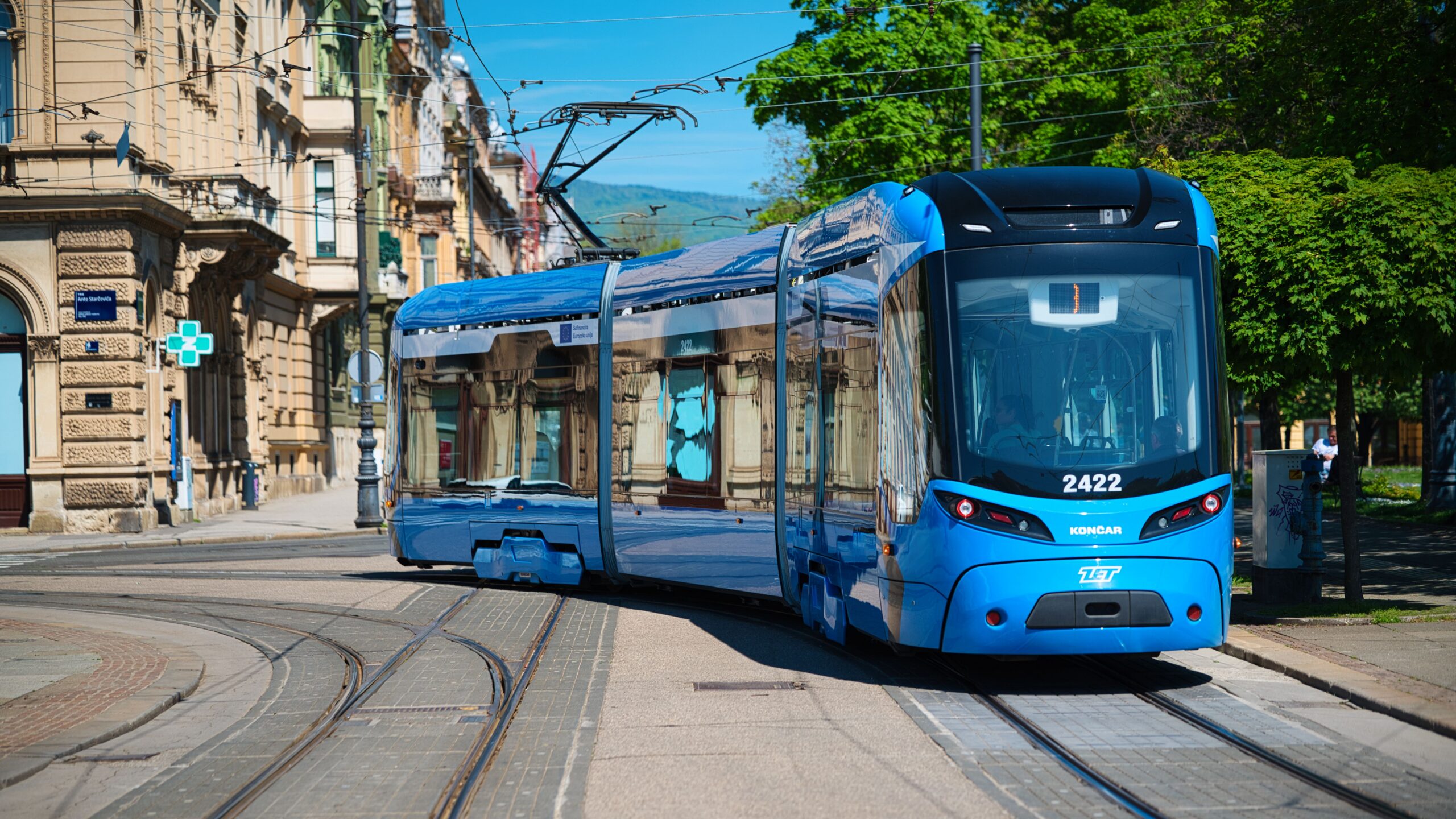 Bright blue tram navigating through a vibrant Zagreb street, showcasing urban transport and architecture.